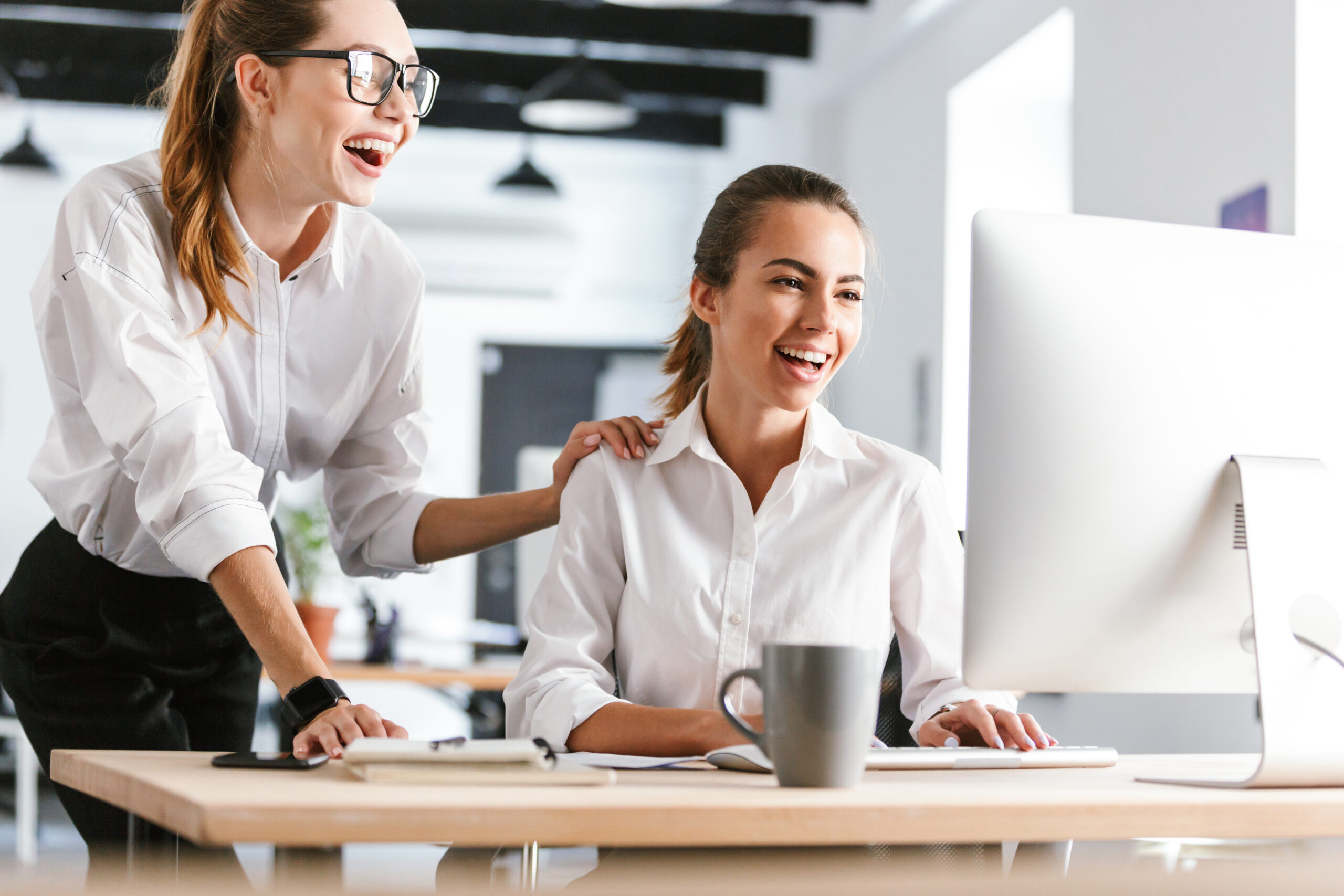 Zwei Frauen haben Freude im Büro und schauen auf einen Bildschirm
